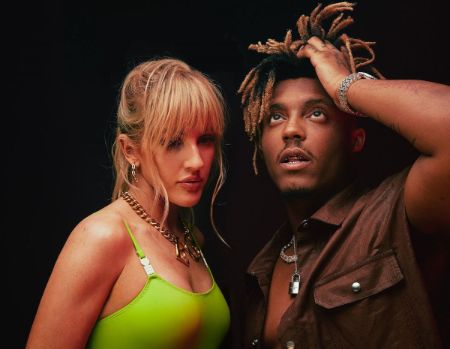 Juice Wrld and British Singer Ellie Goulding standing toegther. Ellie is in a neon top looking down. Juice is in a brown shirt with his hands caressing his hair looking up.